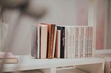 A darker pastel photograph of books lined up on a shelf.