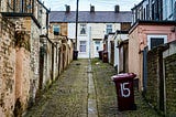 A narrow alley between old terraced houses. Paint crumbles from the bricks, and the neighborhood looks run down.