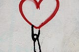 A figure drawn on a wall hangs beneath a heart, like a desperate man hanging from a balloon.