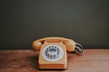 Peach rotary phone on a wood table.