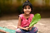 Little Indian girl sitting crosslegged holding a leaf