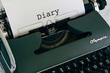 An antique typewriter with a blank page sitting on a writer’s desk.