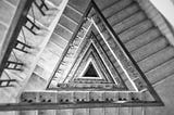 Black and white photo looking down a triangular spiral staircase.