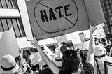 Protesting crowd with one woman holding cardboard sign that says “No hate”