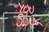 “You suck” written in red on glass