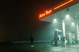 A person standing in the dark outside of a gas station.
