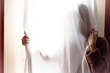 Woman mostly hidden behind white semi-transparent curtain