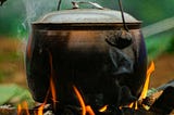 A metal pot suspended on a branch boiling over a naked fire