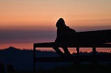 back lit sillohuette of a person on a bench at sunset