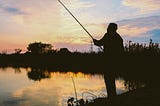 A man fishing at a lake at sunset or sunrise