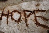 The word “HOPE” scratched into wood, dark letters on light.