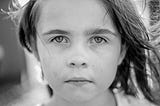 A black and white photo of a child staring back out at the viewer.