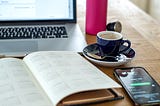 A laptop computer with a schedule, cup of coffee and cell phone on a desk