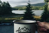 The adventure begins white mug in front of a forest