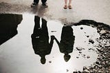A couple watching their reflection in a puddle