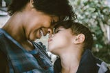 Mother and son, forehead to forehead. The mother is smiling and the son looks peaceful.