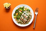 Plate with broccoli and fish on an orange background