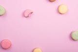 A few macarons laying on a pink surface.