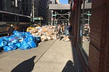 A sidewalk with New York City with a giant pile of clear trash bags taking up most of the sidewalk.