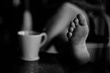 The photo in black and white of a foot on a coffee table, next to a mug.