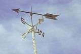 A weather vane against whisps of clouds and blue sky.