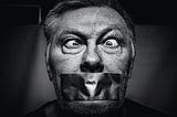 Censorship — A black and white image of an older man, eyes crossed, with duct tape over his mouth.