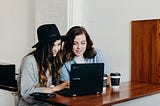 Two girls are sitting in a cafe and working on computer together.