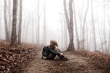 A girl on a hiking trail, sitting down, holding her legs, sad.