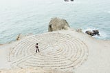 A woman walking in a circular maze created on sand by the beach