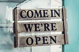 Image of a handmade, handcrafted wood sign that says, “Come In We’re Open”
