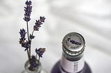 close-up on a couple sprigs of lavender coming out of a vase next to a bottled drink made with lavender