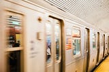 NYC subway rushing through the station. It’s slightly blurry closer to the camera.