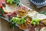 charcuterie board with cheese, meat, bread, grapes, and honey