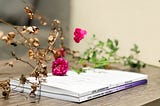 Two white volumes of poetry sitting on a desk, with dried flowers laid on top.