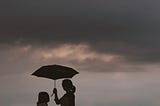 A mother holding a umbrella over her and her daughter on a stormy evening.