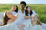 Five international women wearing white dresses in support of the 4B movement sitting and lying on the grass