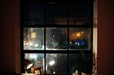 Empty, dark room, looking out through rain blurred glass onto a busy street at night