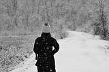 back of person walking into snow-covered woods