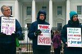 Three protesters in cold-weather gear holding placards against nuclear weapons