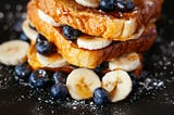 French toast on a black plate, dusted with fruit and sugar.