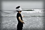 A blindfolded man attempt to look at the ocean.
