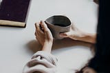 A white table next to a window, a black notebook is lying on the table and the arms and hands of two people sitting opposite each other are visible, one person is holding a mug — kristin_schuhknecht — what would happen to you if you had a regular, mandatory psychologist’s appointment at work? — worklife — job — humanity — astronaut — space — space exploration — future