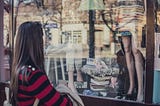 woman looking in the window of a shop that sells clothing and books