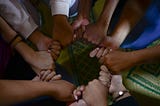 A circle of diverse hands clasped together in a powerful symbol of community, illustrating the shift from a lonely individual perspective to the strength of a collective ‘we’.