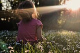 A little girl sitting on the grass enjoying the shining sun.