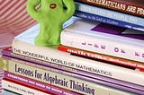 A green creature made of clay stands on a stack of math and logic books and appears to be distressed.