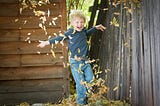 Laughing child kicking up a shower of golden crisp autumn leaves which form a heart around him