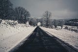 Country road with snow on each side and naked trees