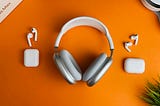 Two pairs of white earbuds laid down on an orange surface with a white headphone in between them.