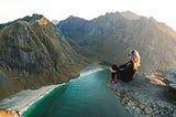Woman sitting on edge of rock overlooking mountains and seaside